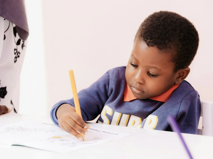 Young boy drawing with a yellow pencil at a table